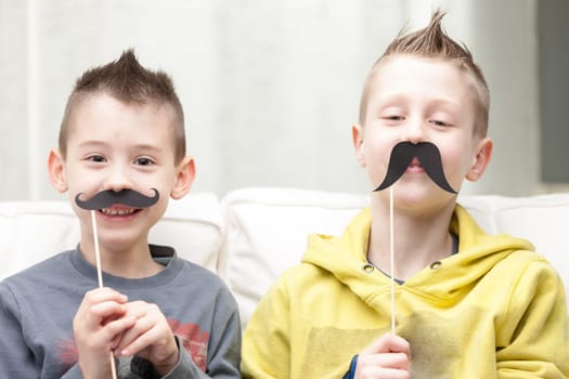 couple of little brothers making funny faces with fake moustaches