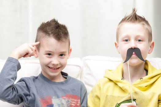 couple of little brothers making funny faces with fake moustaches