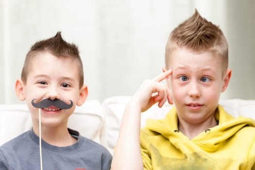 couple of little brothers making funny faces with fake moustaches