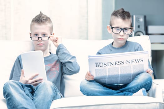 Spoof of two young boys wearing glasses posing as businessmen as they sit side by side on a sofa reading the Business Times and using a tablet