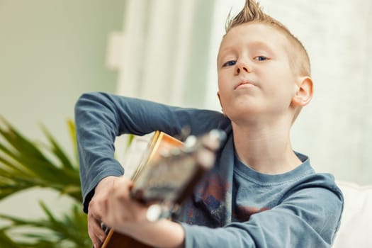 Young boy playing his guitar for the camera in a close up portrait conceptual of childhood hobbies and talent