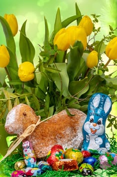 Easter card template. A traditional Easter lamb cake with ribbon and an Easter bunny and many  other chocolate sweets over yellow tulip bunch background. Macro.
