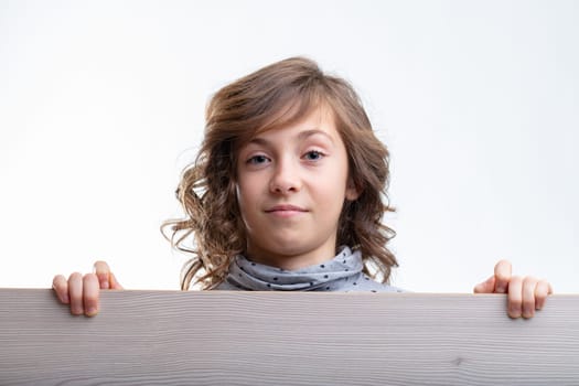 Young girl looking over the top of a wooden board with a quiet smile and thoughtful expression isolated on white