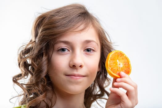 Pretty little girl holding up a slice of fresh orange rich in Vitamin C with a pleased smile in a healthy diet and nutrition concept isolated on white