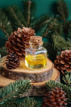 Glass bottle with conifer essential oil near fir branches and pine cones on wooden piece on green close up. Aromatherapy, spa and herbal medicine concept. Natural remedy or cosmetics.