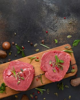 Raw beef fillet steaks on wooden board on dark table close up with copy space. Portioned filet mignons with spices and herbs. Concept of summer food