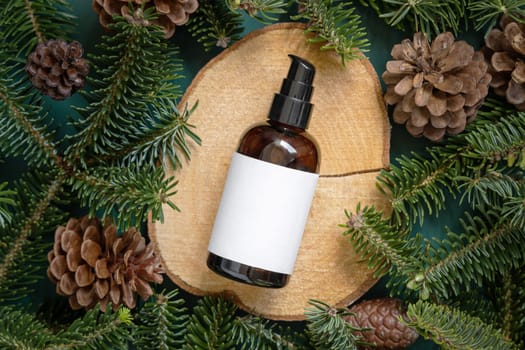 Brown glass bottle between fir branches and pine cones on wooden piece top view. Brand packaging mockup. One pump dispenser for skincare product, cream or serum. Healthcare concept. Natural cosmetics.