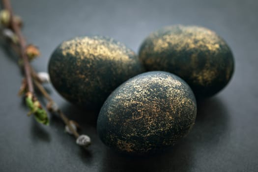 Easter painted eggs with gilding in partial out of focus on a table with a willow branch.