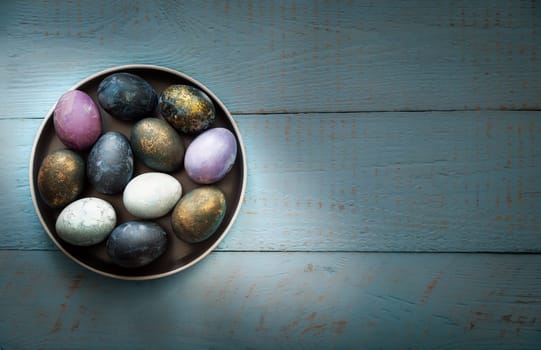 Easter colored eggs in a dish on a blue wooden background. Place for text.