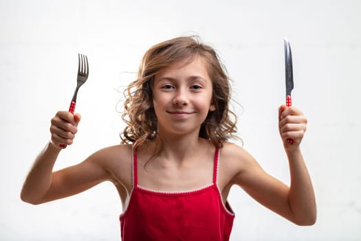 Playful young girl holding up a knife and fork in her hands with a mischievous smile isolated on white