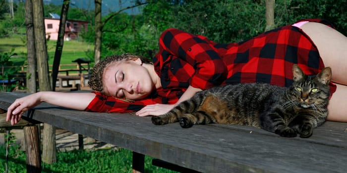 gorgeous woman with braided hairstyle, languidly lying with her eyes closed on the table, just like the cat who is with her in the same attitude