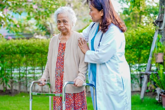 Doctor help Asian elderly woman disability patient walk with walker in park, medical concept.