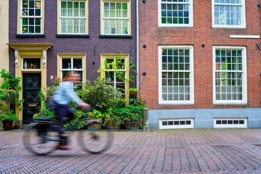 Motion blurred bicycle rider cyclist man on bicycle very popular means of transport in Netherlands in street with old houses of Delft, Netherlands