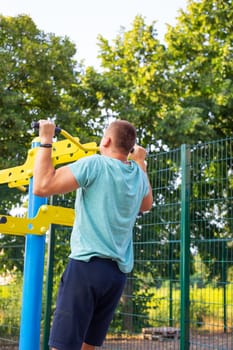 A man is exercising on the street. Opening gym outdoors on the sports ground in a green park