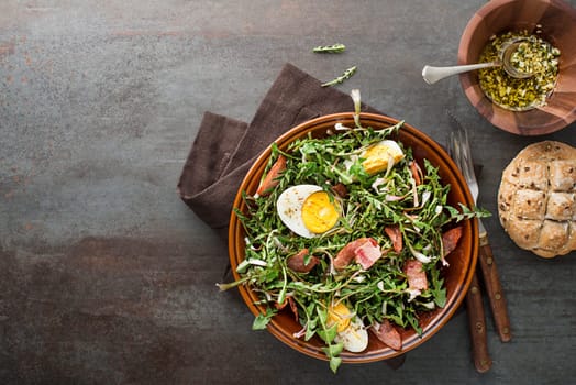 Dandelion salad with eggs and bacon on grey background