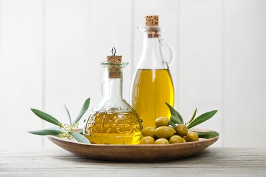 Olive oil bottles with green olives fruit and olive branch on wooden table