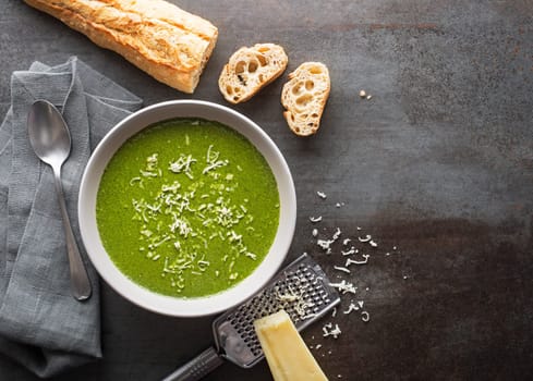 Fresh vegetable cream soup with parmesan cheese on grey background overhead shoot.