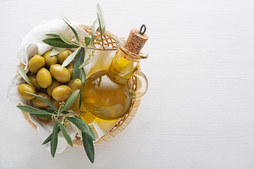 Olive oil bottle and olives with branch in basket on wooden table