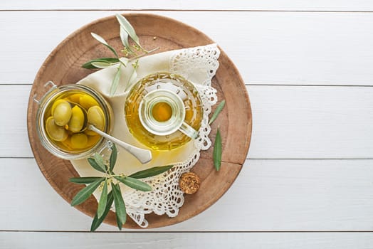 Olive oil bottle and olive branch with Pickled green olives in glass jar on wooden table