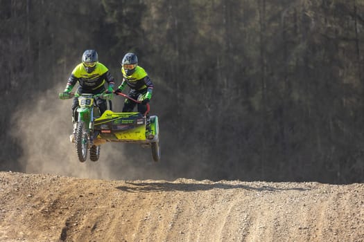 MOHELNICE, CZECH REPUBLIC - APRIL 16, 2022. Sidecacross riders jump with motorbike on a dark background in the "Sidecarcross Championship of Czech Republic"" on April 16, 2022 in Mohelnice, Moravia, CR"