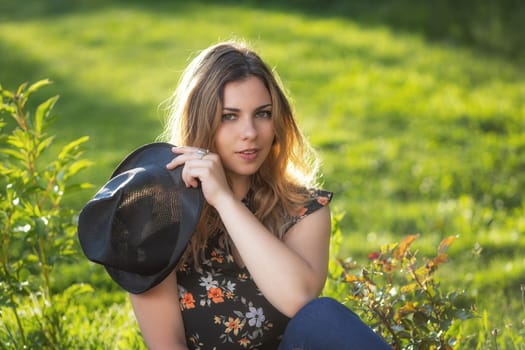 Portrait of attractive  young woman iposing with her black  straw hat outdoors. Horizontally.