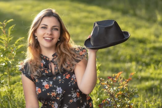 Portrait of smiling attractive  young woman showing her black  straw hat. Horizontally.