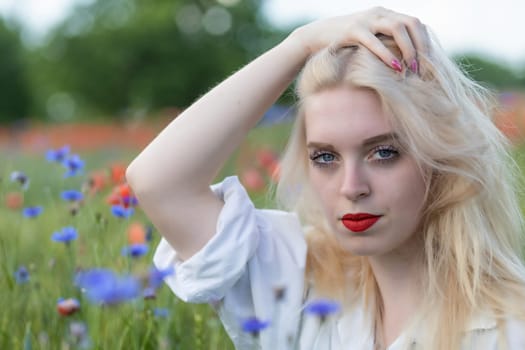 Front view portrait of sad blonde woman in cornflower and poppy meadow. Horizontally.