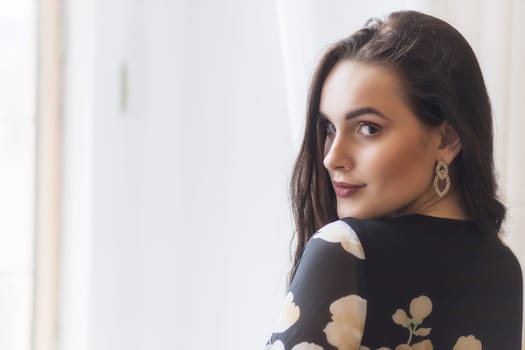 Dark haired young woman is looking over her shoulder indoors. Horizontally.