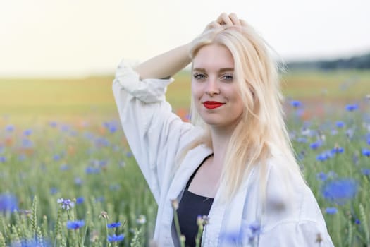 Smiling attractive blonde woman with hand in hair in cornflower and poppy meadow. Horizontally.