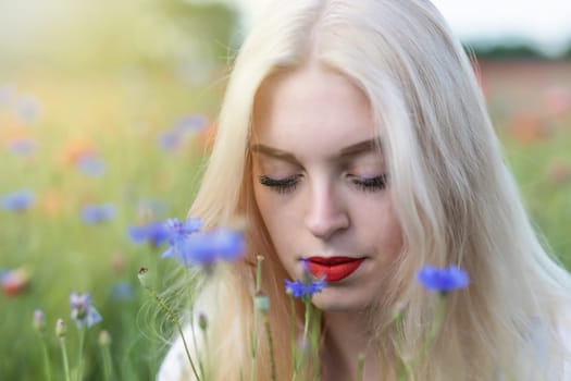 Closeup portrait of attractive blonde woman in cornflower and poppy meadow. Horizontally.