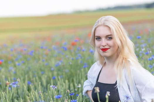 Smiling attractive blonde woman in cornflower and poppy meadow in summer day. Horizontally.
