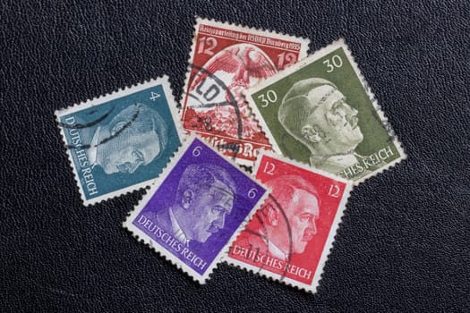 Potsdam, Germany – APR 20, 2022. Old German stamps from the Third Reich, with the printed portrait of Adolf Hitler and one from the 1935 Reich Party Congress of the NSDAP on a black leather background. Macro.