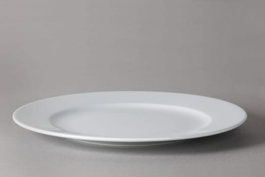 A flat front angle view of a white dinner plate on neutral background with shadow