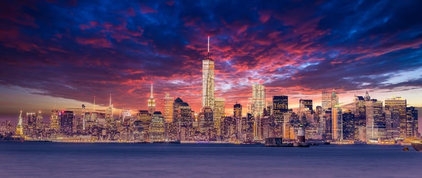 New York City Manhattan downtown skyline at dusk with skyscrapers illuminated over Hudson River panorama. Dramatic sunset sky