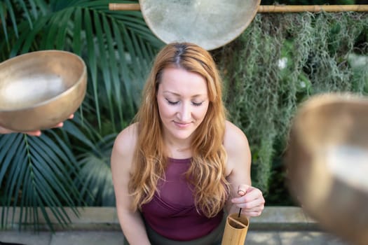Yoga concept, meditation and sound therapy. Beautiful young caucasian woman surrounded by copper tibetan singing bowls and instruments