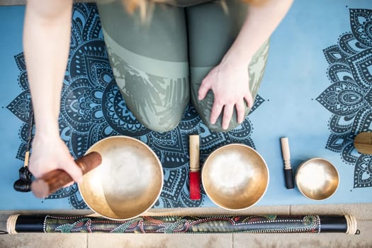 Yoga concept, meditation and sound therapy. Beautiful young caucasian woman surrounded by copper tibetan singing bowls and instruments