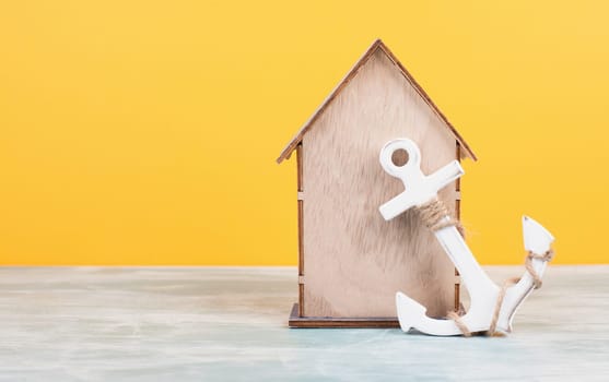 Wooden house with an anchor, yellow background, buying or renting a house, real estate concept, booking home for vacation, copy space for text