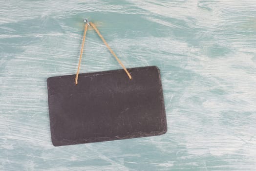 Black chalkboard sign is hanging on a blue textured background, weathered door, welcome and sale concept, copy space for text