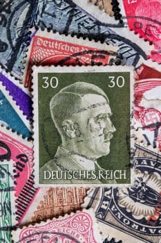 Potsdam, Germany - APR 26, 2022. A stack of old German stamps from the Third Reich and on it a stamp with printed portrait of Adolf Hitler, the leader of NSDAP party. Macro.