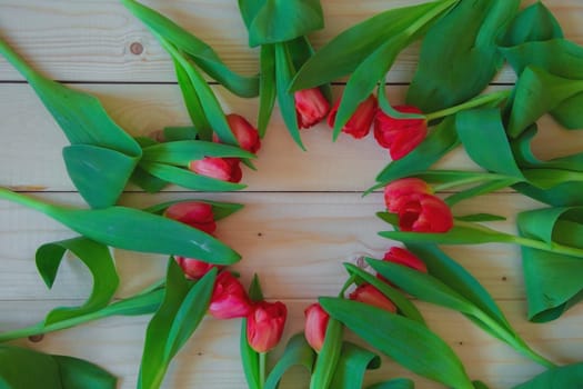 Pink tulips with green leaves lie in a circle with a free place in the center on a wooden background. High quality photo