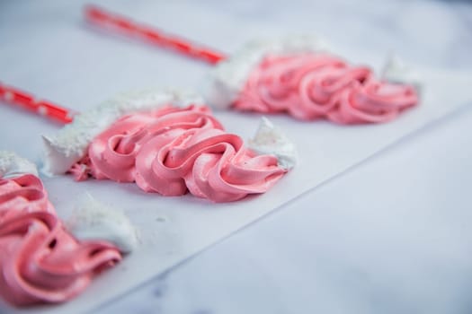 Meringue in the form of pink Christmas hats, with a white bumbone and rim lies on white parchment. High quality photo