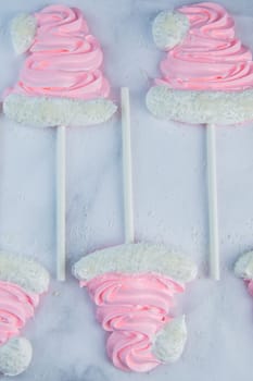 Meringue in the form of pink Christmas hats with a pompom and a white lapel on a stick lie on white parchment in two rows. High quality photo