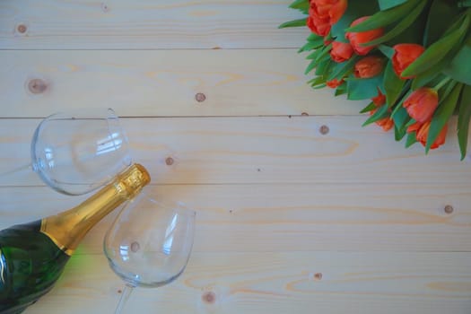 Pink tulips with green leaves lie in the upper corner on a wooden background, and opposite in the lower corner are wine glasses. High quality photo