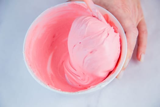 Pink confectionary meringue marengo is mixed in a white bowl on a white marble background by the hands of a pastry chef. High quality photo