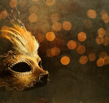 Golden venetian mask over shiny bokeh background with golden texture