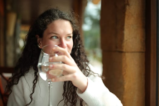 Happy woman holding glass of water looks through window
