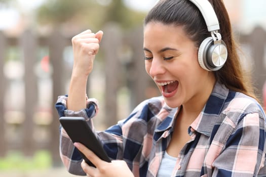 Excited teen with headphones checking smart phone