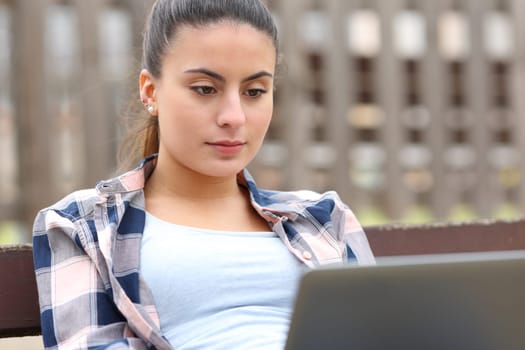 Teen checking laptop content sitting on a bench