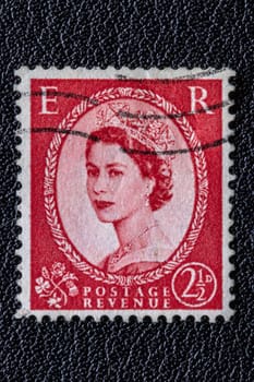 Potsdam, Germany - APR 26, 2022. A old of Great Britain (United Kingdom) issued stamp with portrait of Queen Elizabeth II with postmark on a black leather background. Stamp 2 1/2p, Scarlet. Ca. 1952