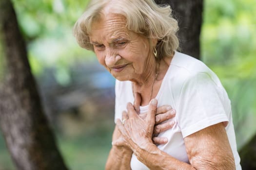 Elderly woman outdoors with heart pain holding her chest